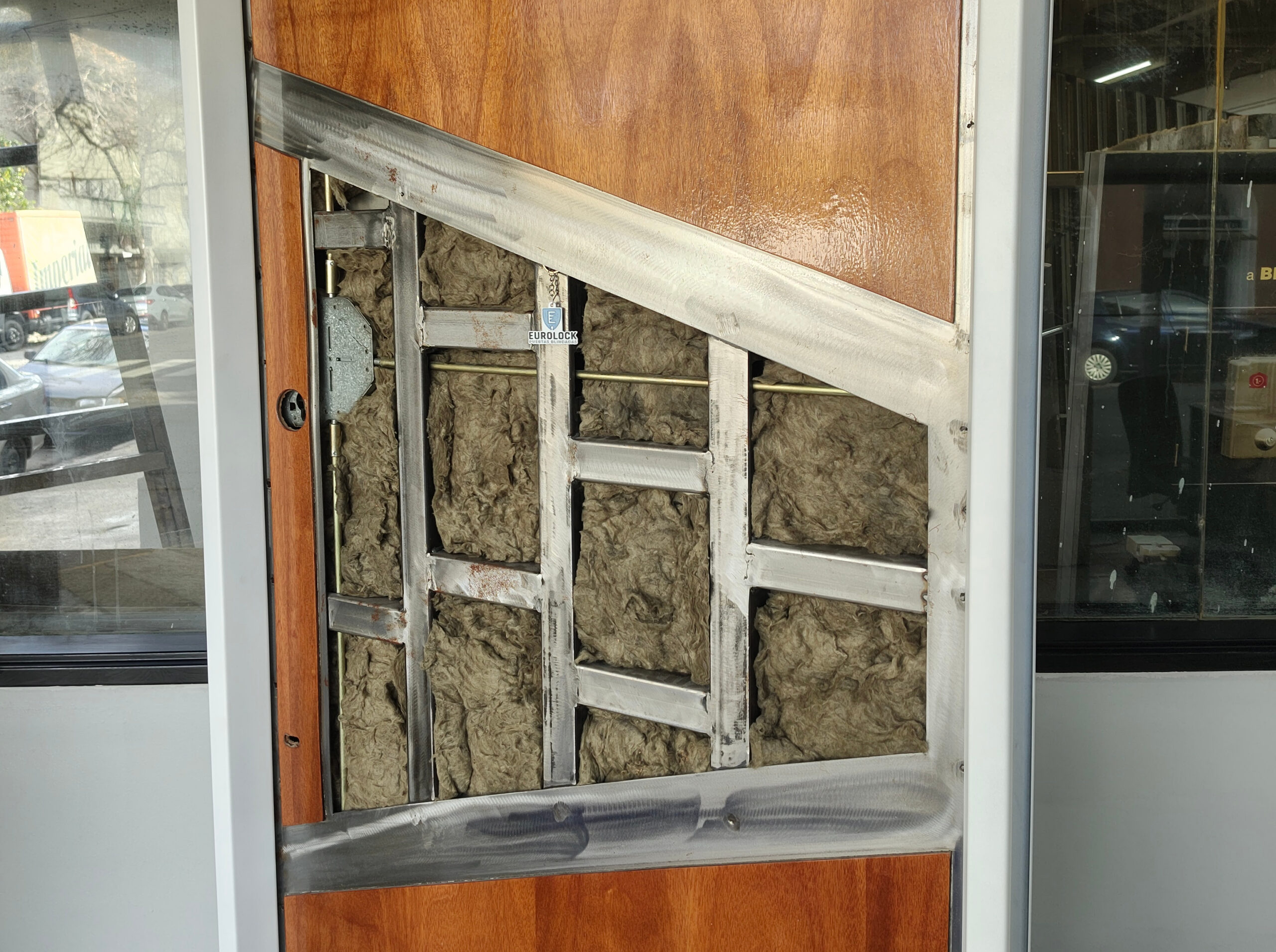 Interior de una puerta blindada: bastidor de acero con refuerzos, barras de cierre multipunto y relleno de lana de roca para aislamiento.